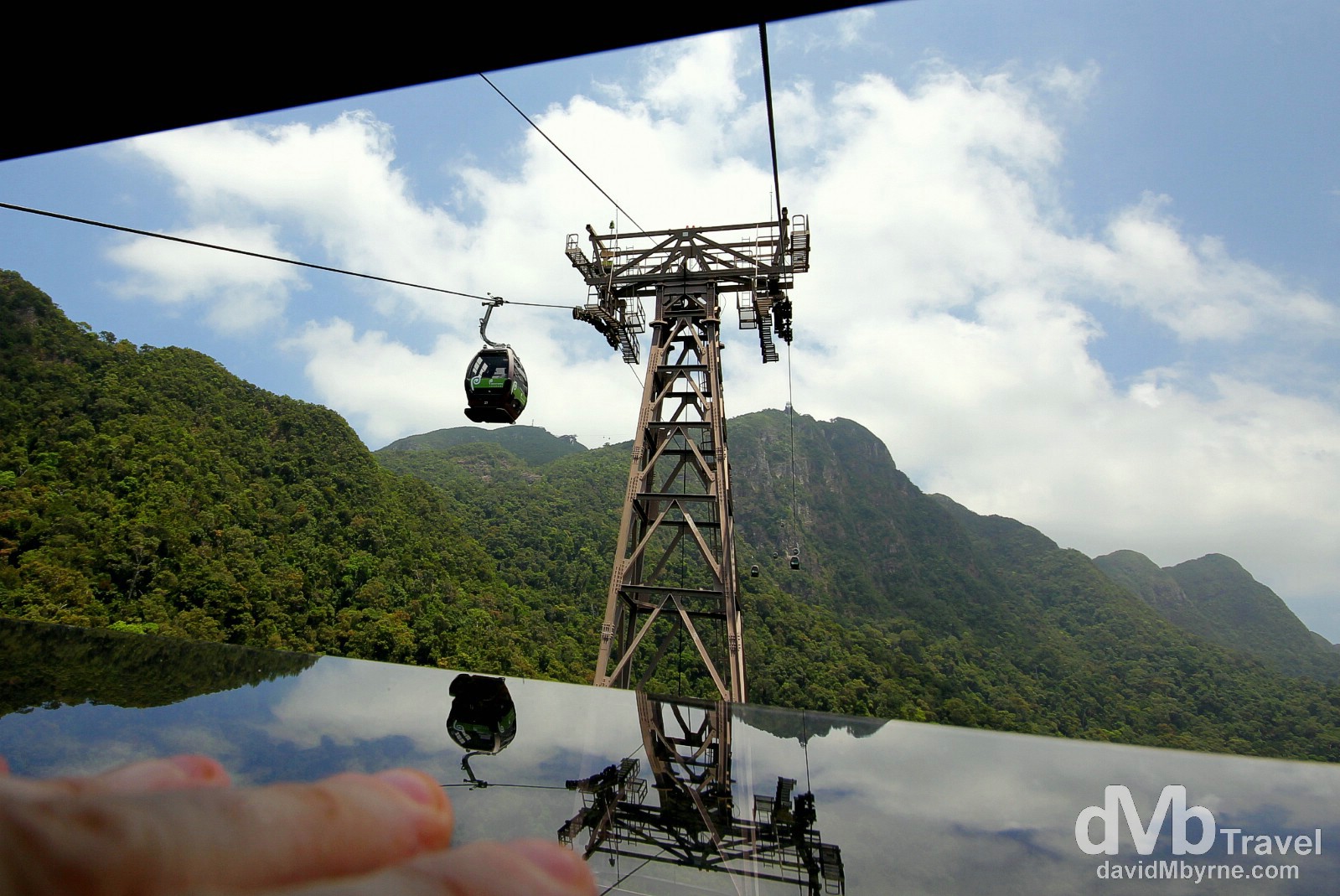 This is a picture taken through a narrow cap in a window of the Langkawi Cable Car, the most popular tourist attraction on the island. I was ascending when I took this & needed to keep the spring-mounted window open with my left hand (bottom left) while holding the camera with my right. I’m a sucker for reflections so of course I particularly like the reflections seen here; I feel they detract from the poor mountain visibility caused by low-lying haze emanating from, I assume, the jungle floor below. In the distance, beyond the mammoth 70m-high Tower 2 as seen here, is the longest free span section of the whole 2.2km cable car ride, the 950m stretch between the tower up to the Middle Station. Gunung Machinchang, Langkawi Island, Malaysia. March 22nd 2012.