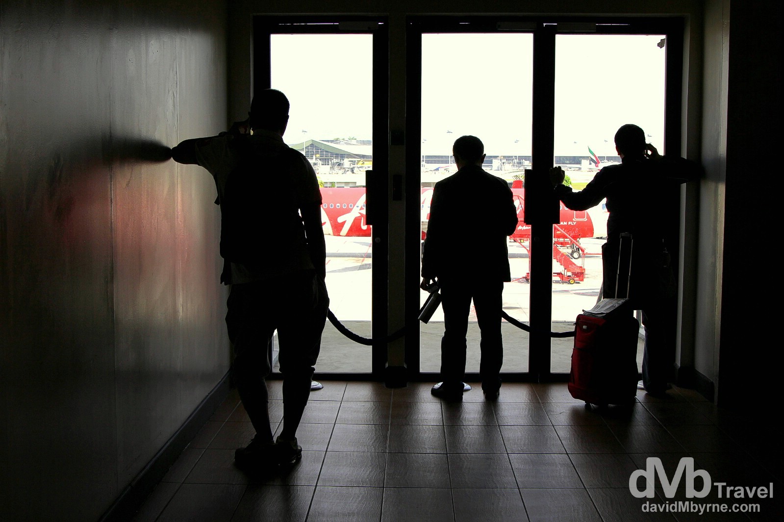 Silhouettes of transit travellers looking out onto the tarmac from the departures terminal of Kuala Lumpur International Airport, Kuala Lumpur, Malaysia. March 6th 2012.